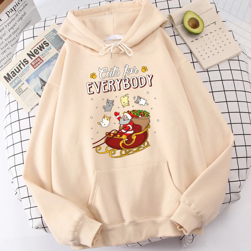 Beige hoodie with "Cats for Everybody" text and Santa Claus in a sleigh with playful cats. Includes a newspaper, an avocado, and a notepad on a checkered background.