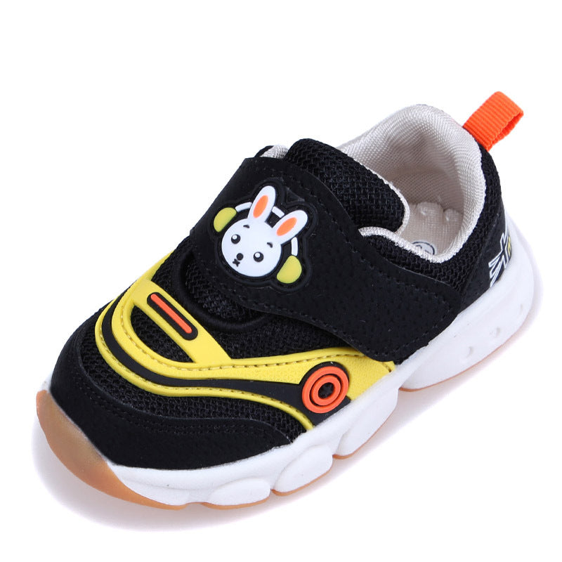 Children's sneaker with a playful black and yellow design, featuring a cartoon rabbit on the strap. It has a breathable mesh upper, a white sole, and an orange pull-tab at the heel.