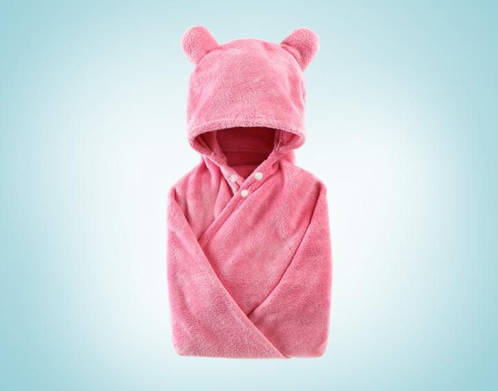 Pink baby blanket with a hood featuring bear ears and button closures, set against a gradient light blue background. The fabric appears soft and plush.