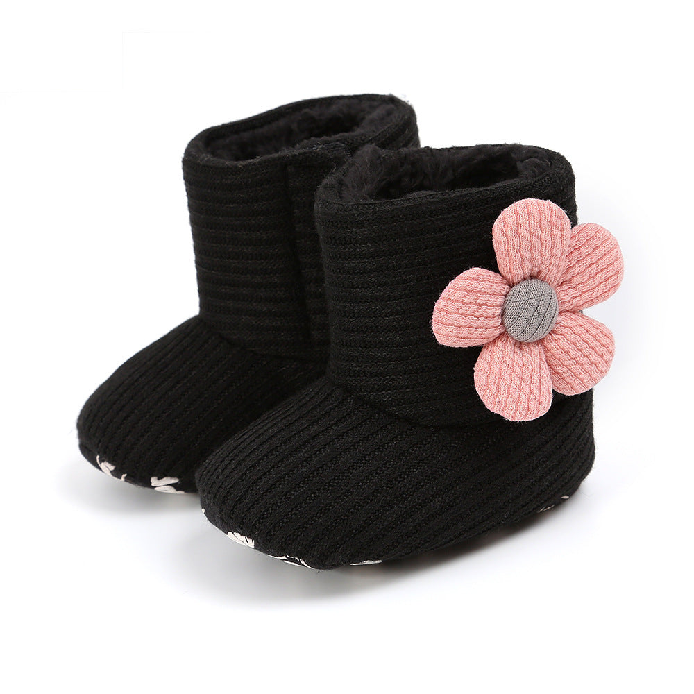 Black ribbed baby booties with a large pink flower decoration on the side. The boots have a soft, cozy appearance suited for infants.