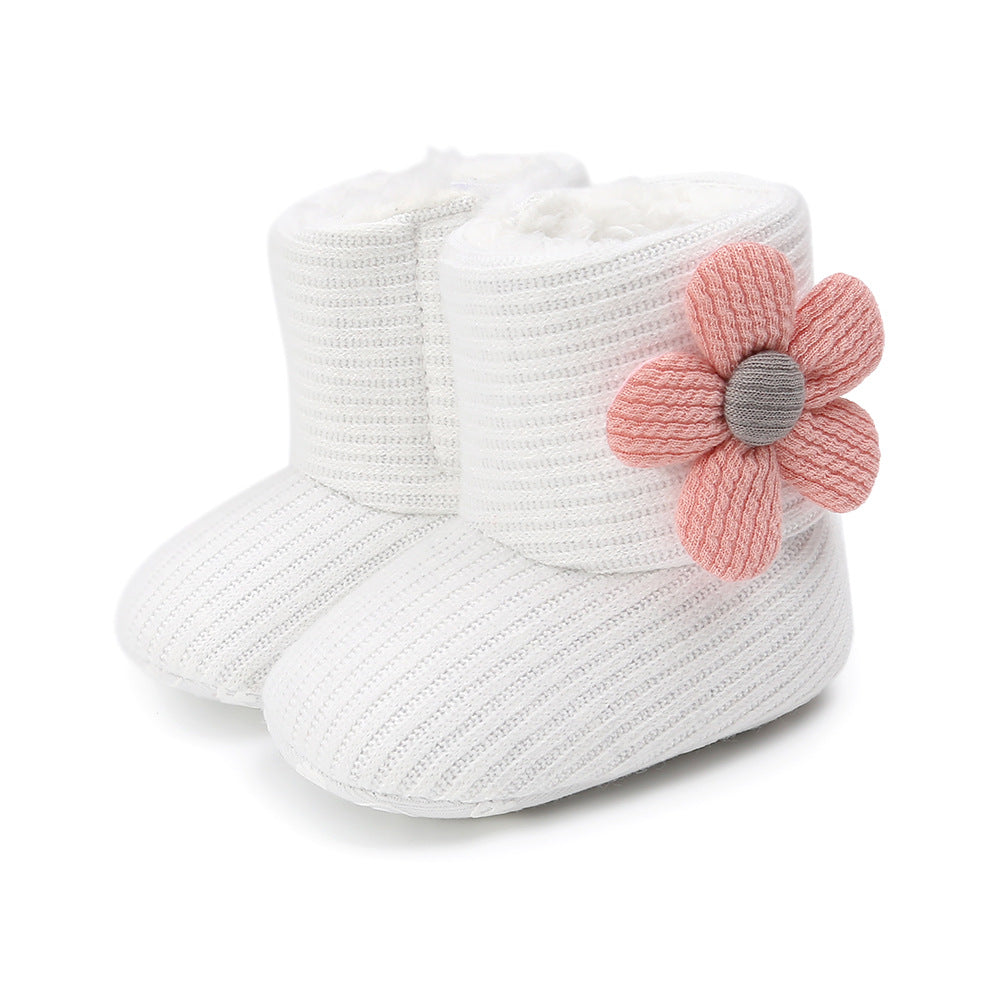 White knitted baby booties with ribbed texture, featuring a cute pink and gray fabric flower on the side.