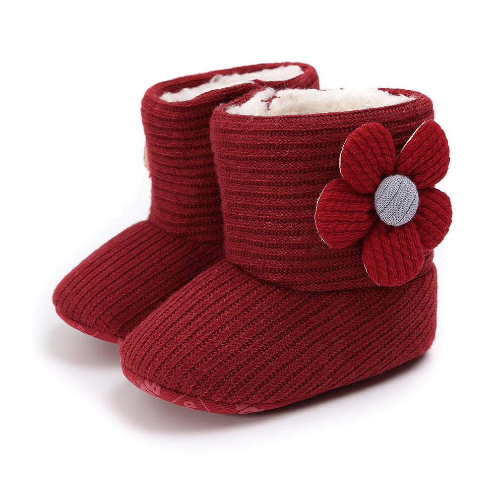 Red knitted baby booties with a textured pattern, featuring a side flower embellishment. They have a soft, plush lining for warmth and comfort.