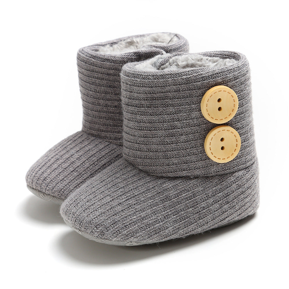 Gray knitted baby booties with ribbed texture, featuring two beige buttons on the side. Soft, cozy interior ideal for warmth and comfort.