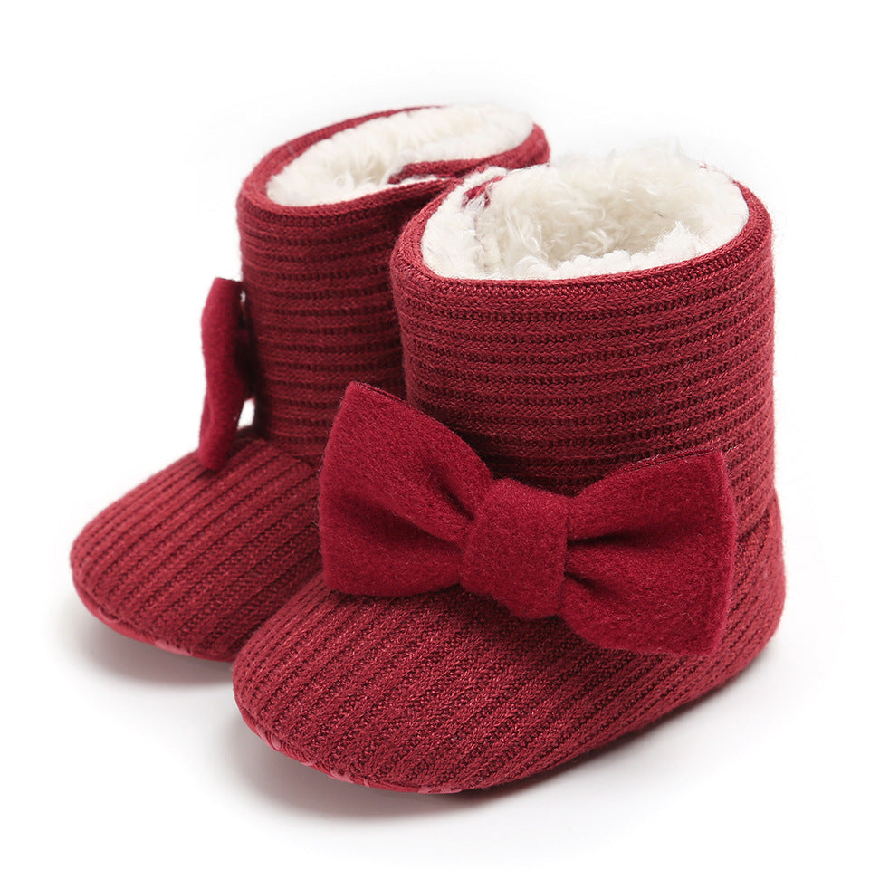 Red knitted baby booties with a large bow and soft white lining, featuring a ribbed texture.