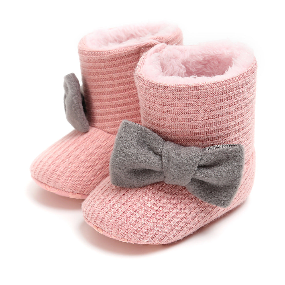 Pink knitted baby booties with a ribbed texture and plush interior. Each bootie features a large gray bow on the front, providing a soft and cozy appearance.