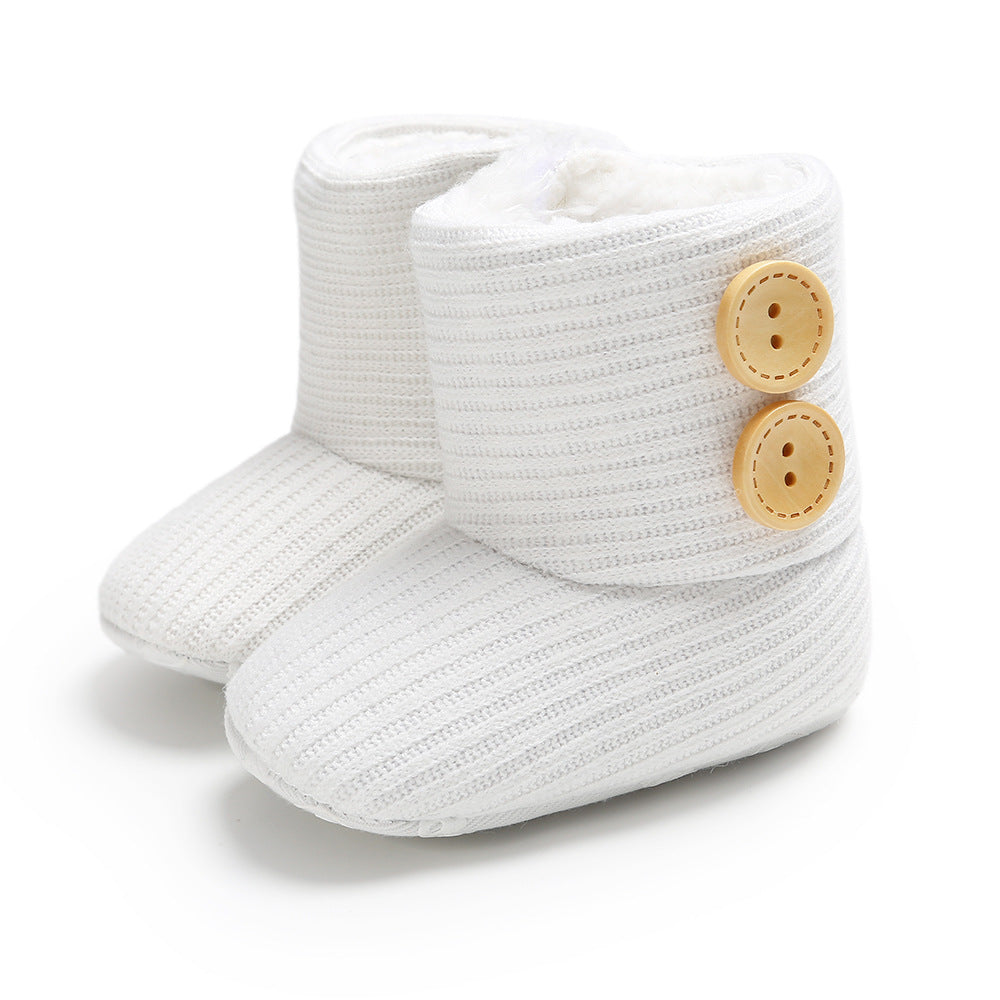 White knit baby boots with ribbed texture and two tan wooden buttons on the side. The boots have a soft, plush lining.