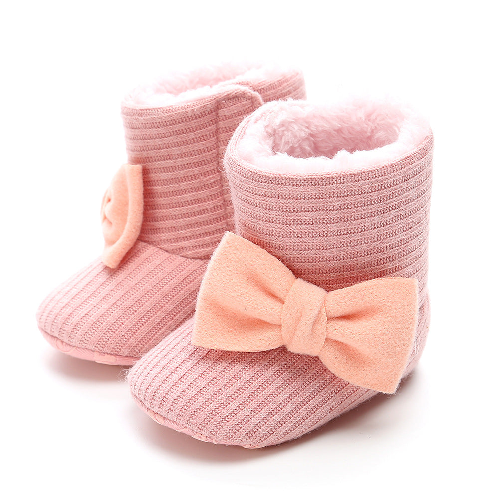 Pink knitted baby booties with soft, fluffy lining and a large peach bow on the side, placed on a white background.