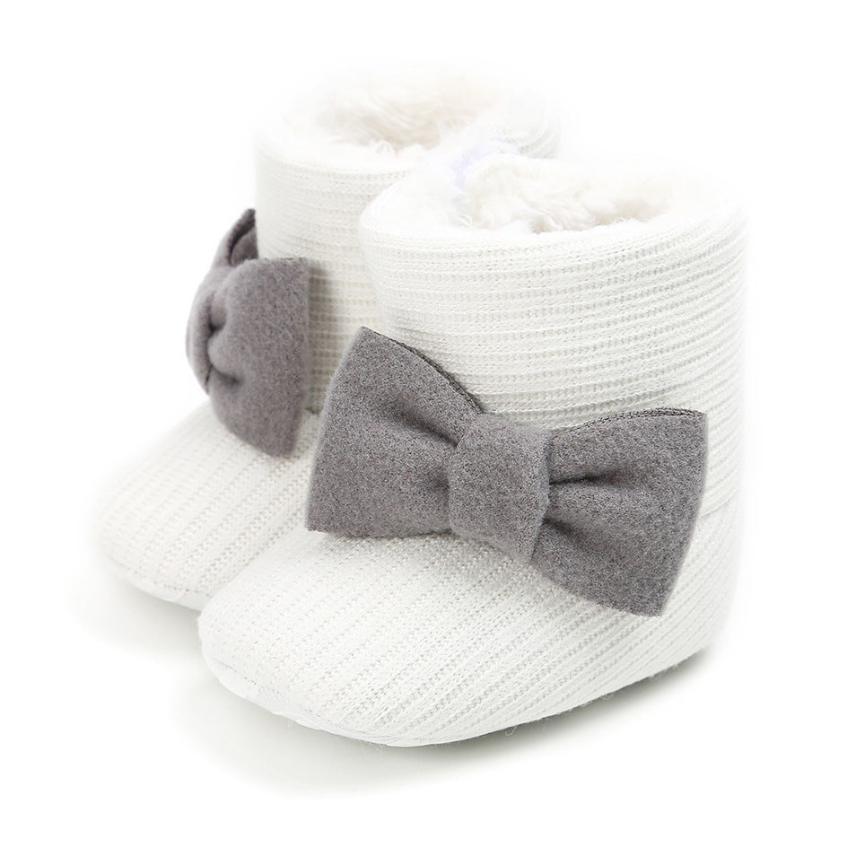 White infant booties with a knitted texture, featuring soft, fluffy lining and adorned with large gray felt bows on the sides.