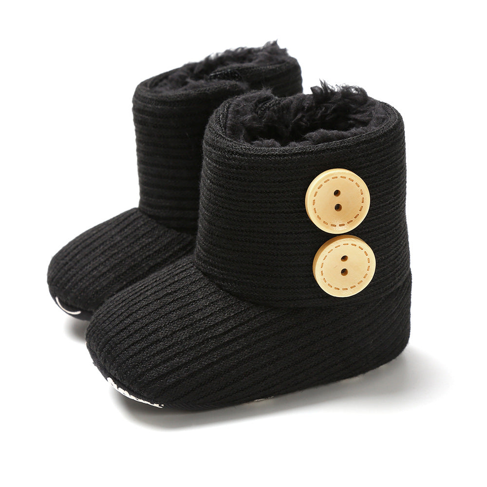 Black knitted baby boots with a ribbed texture and two large beige buttons on the side. The interior is lined with soft black fur for warmth.