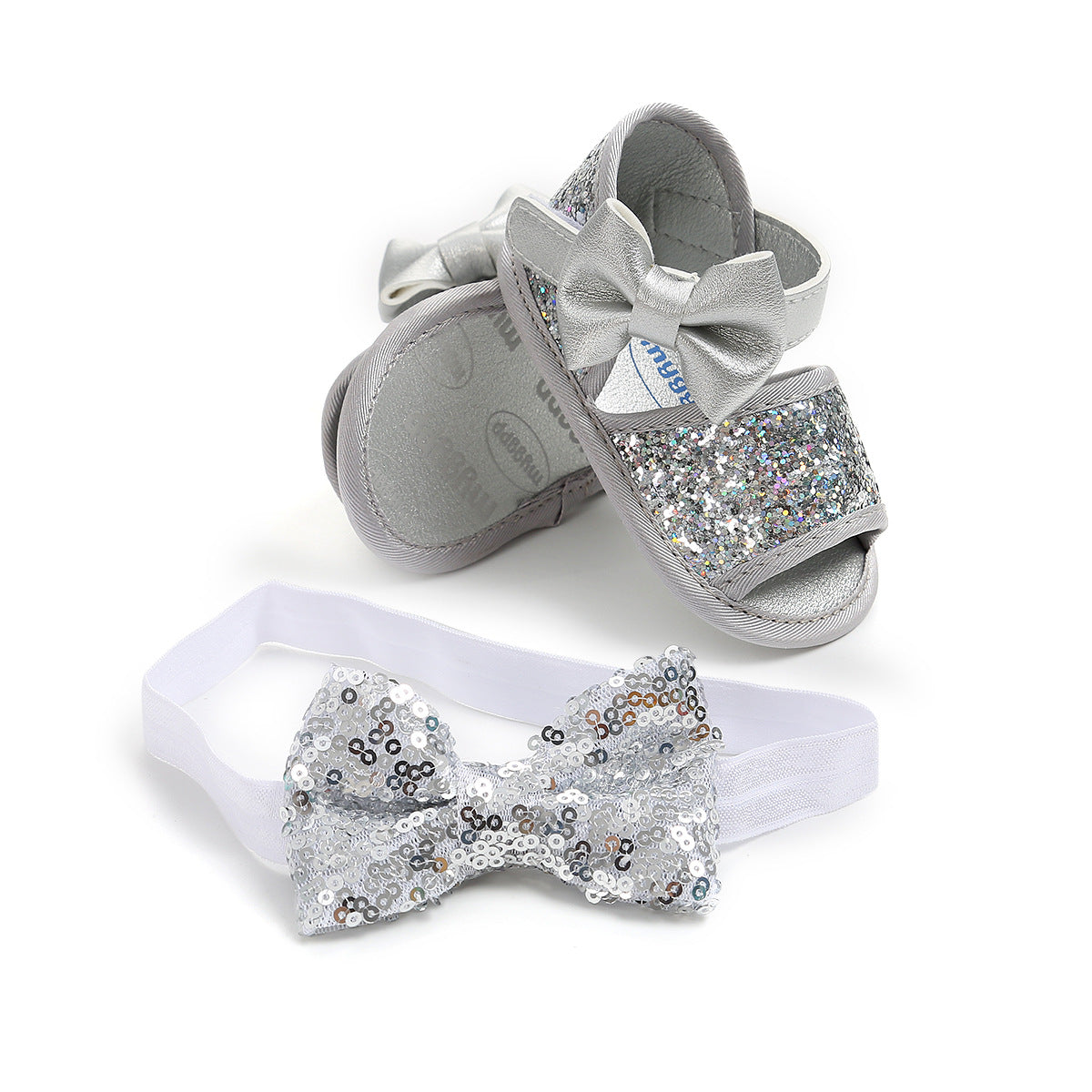 Silver baby sandals with glittery straps and bows paired with a matching sequined bow headband on a white background.