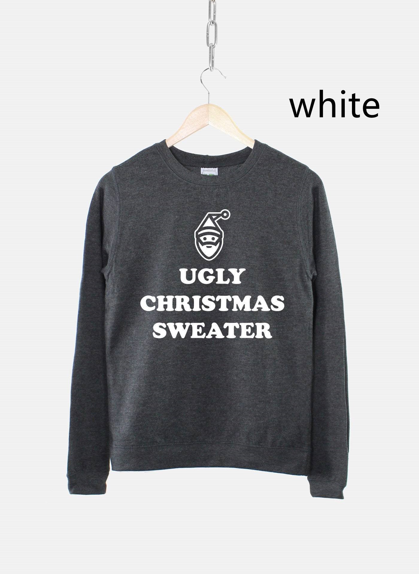 Dark gray sweatshirt with "UGLY CHRISTMAS SWEATER" text and a simple outline of a gnome face in white, hung on a wooden hanger. The word "white" is also shown to the right.