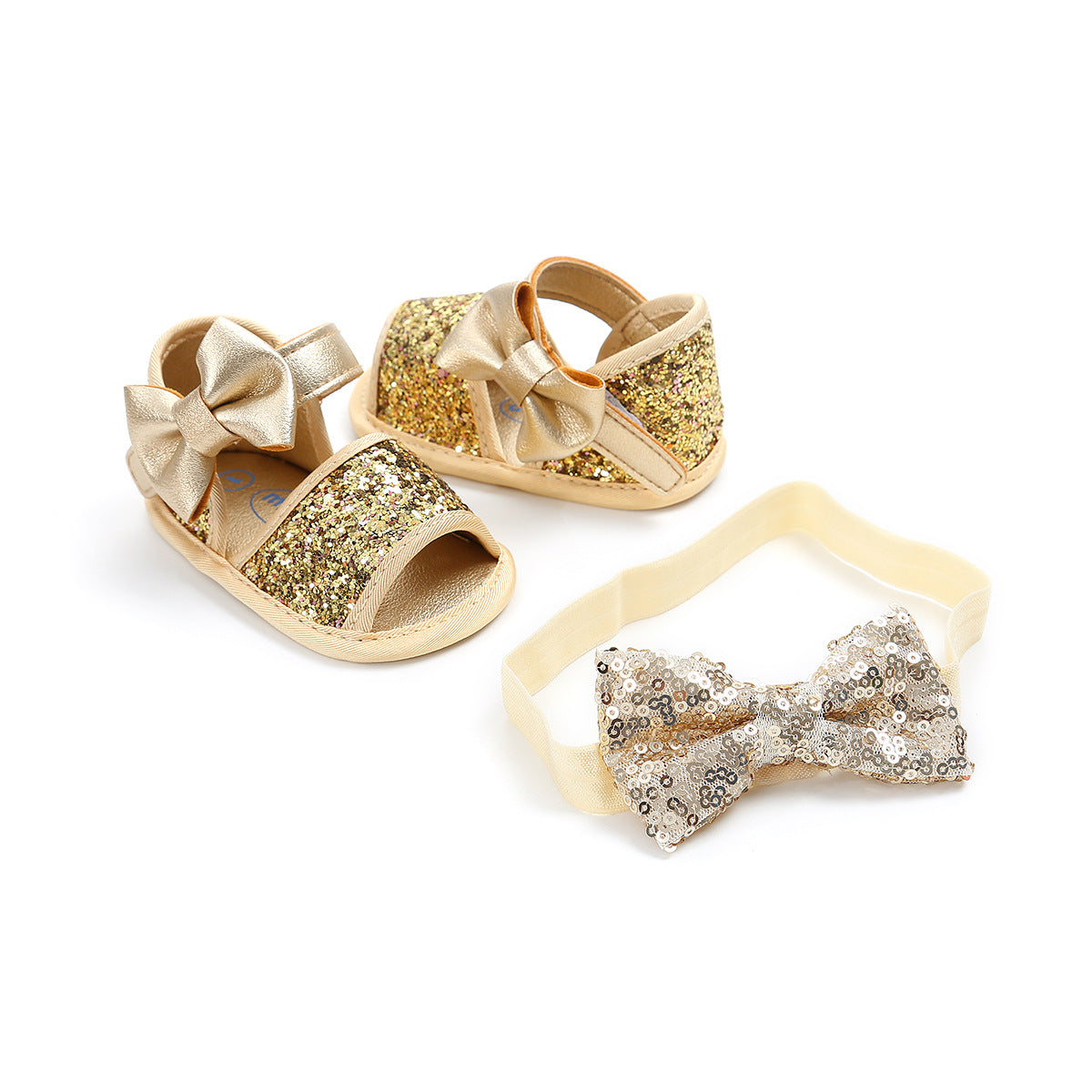 Golden glittery baby sandals with matching bows are paired with a sequin-studded headband featuring a large bow. The set rests on a plain white background.