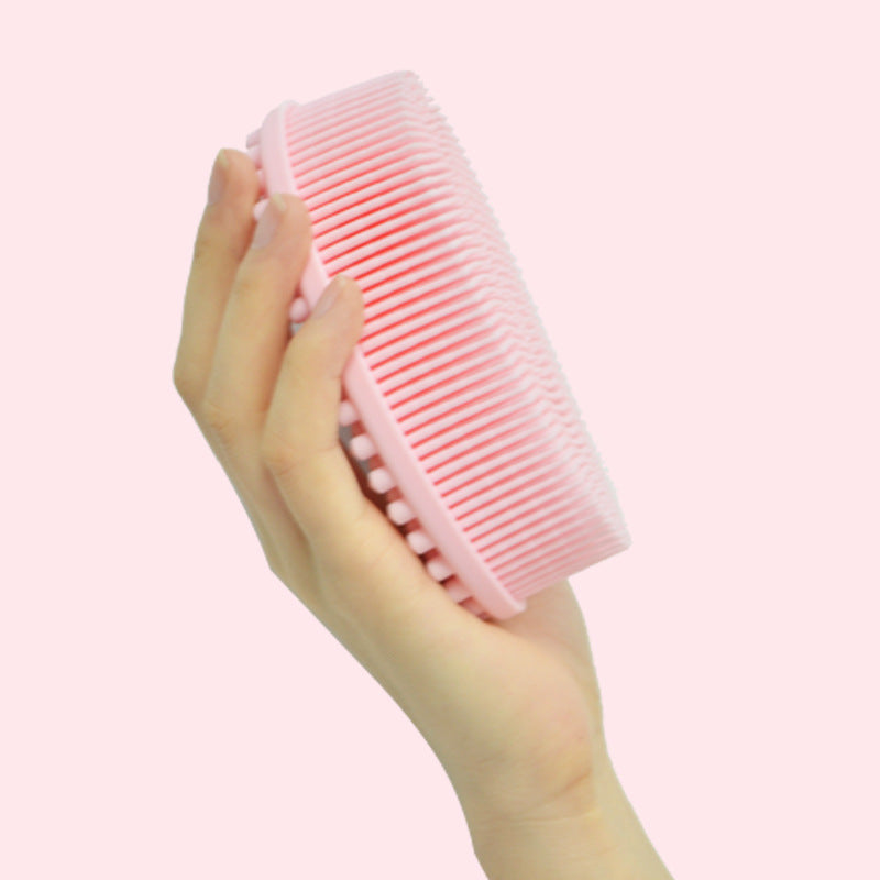 A hand holding a round pink silicone scrubber with soft bristles against a pale pink background.