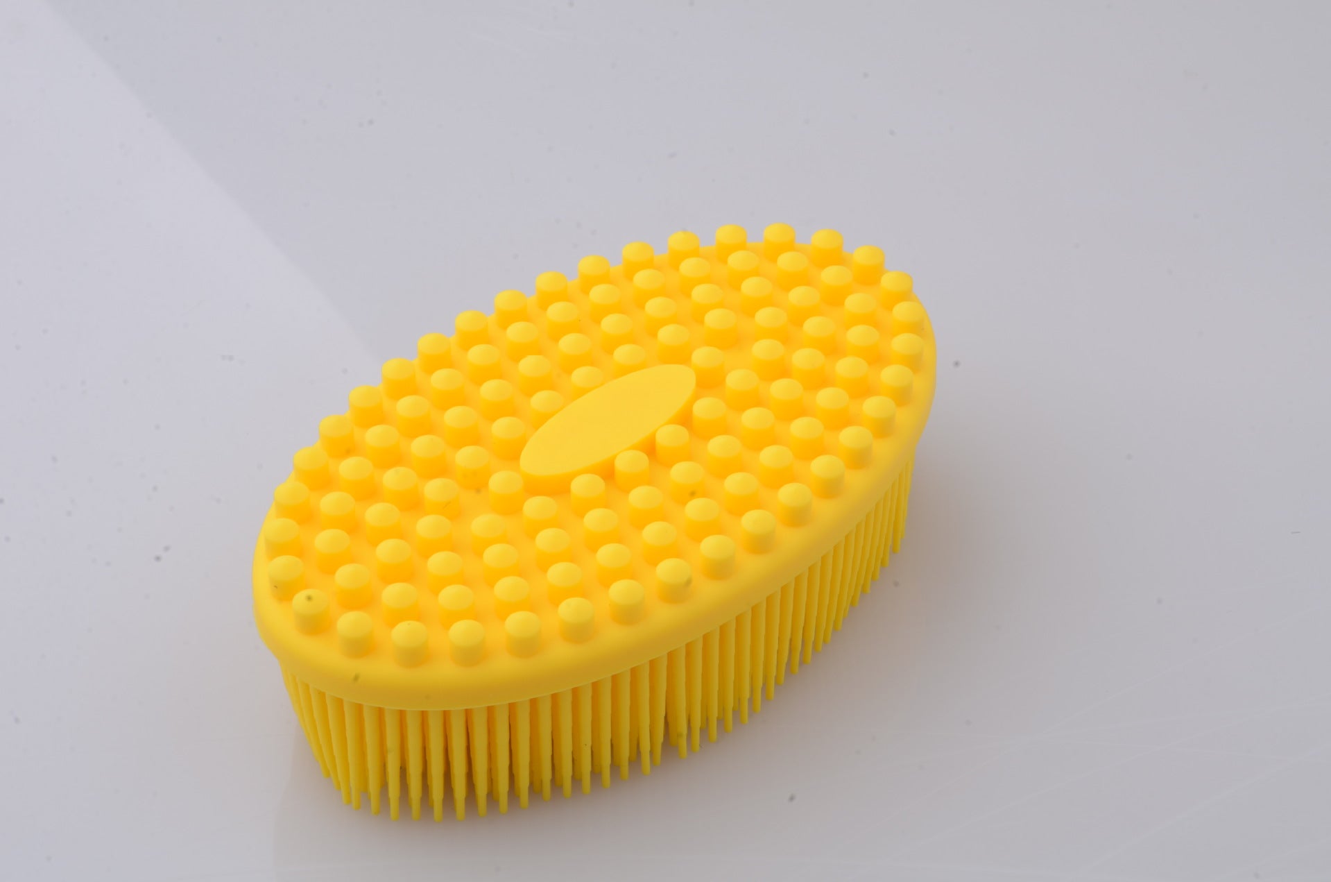 Yellow oval studded bristle brush on a light background, featuring round bumps on top and fine bristles beneath, designed for cleaning or massaging purposes.