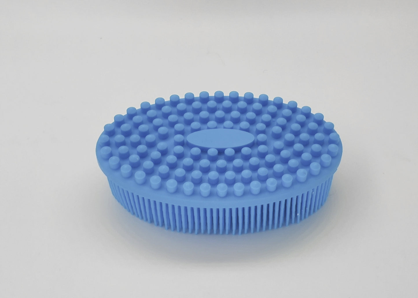 Blue oval silicone scrubber with short bristles on the bottom and rounded nubs on the top, designed for exfoliating or cleaning purposes, placed on a white background.