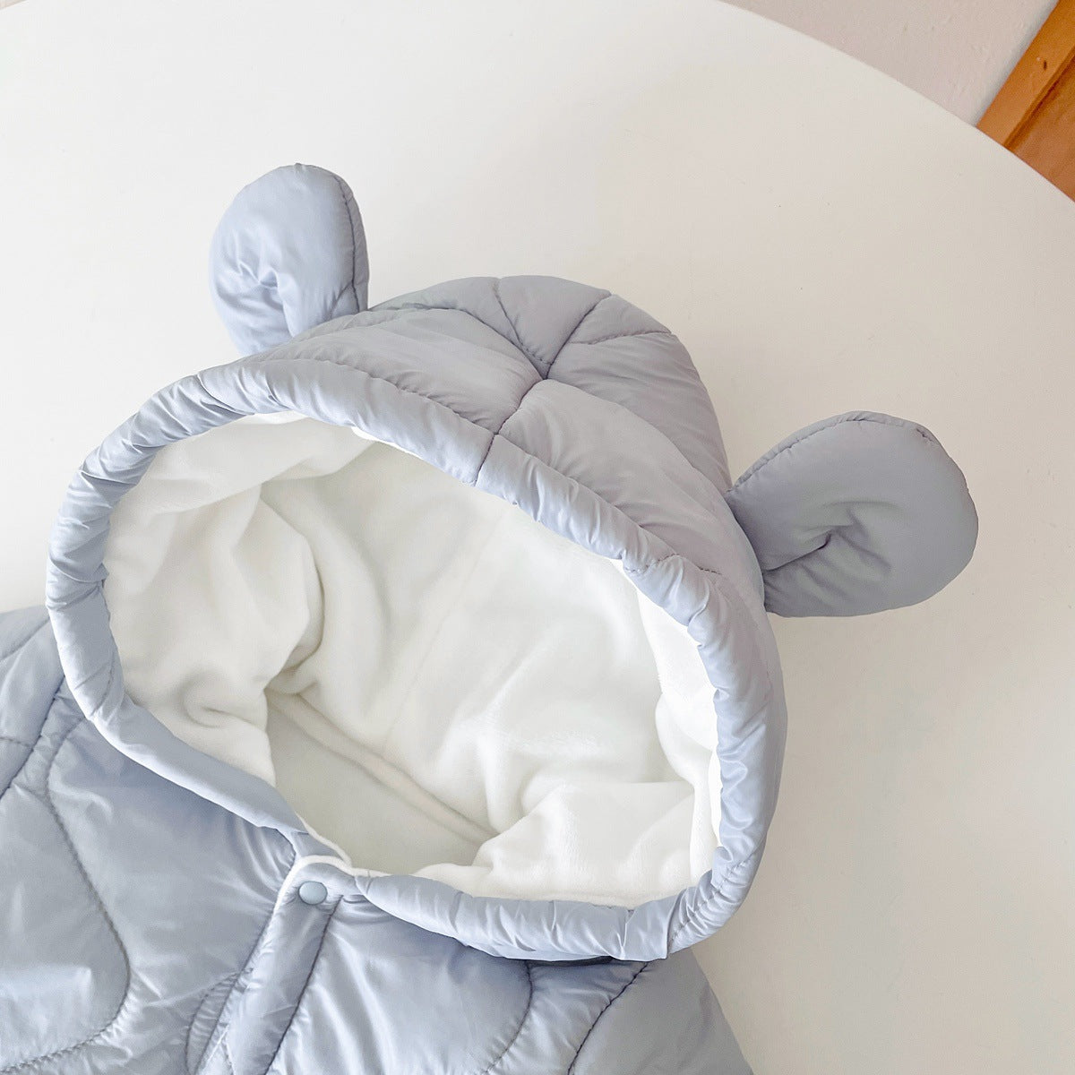 Light gray hooded jacket with soft white lining, featuring fabric ears on the hood, laid on a white surface.