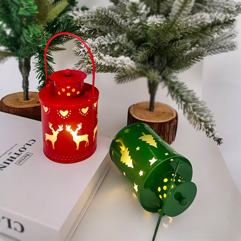 Festive red and green lanterns with reindeer and tree cutouts casting warm light. They are set on a white surface with snow-covered pine decor behind them.