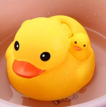 A large yellow rubber duck with a red beak floats in a peach-colored tub, accompanied by a smaller duckling on its back. Both ducks have large, black cartoon eyes.