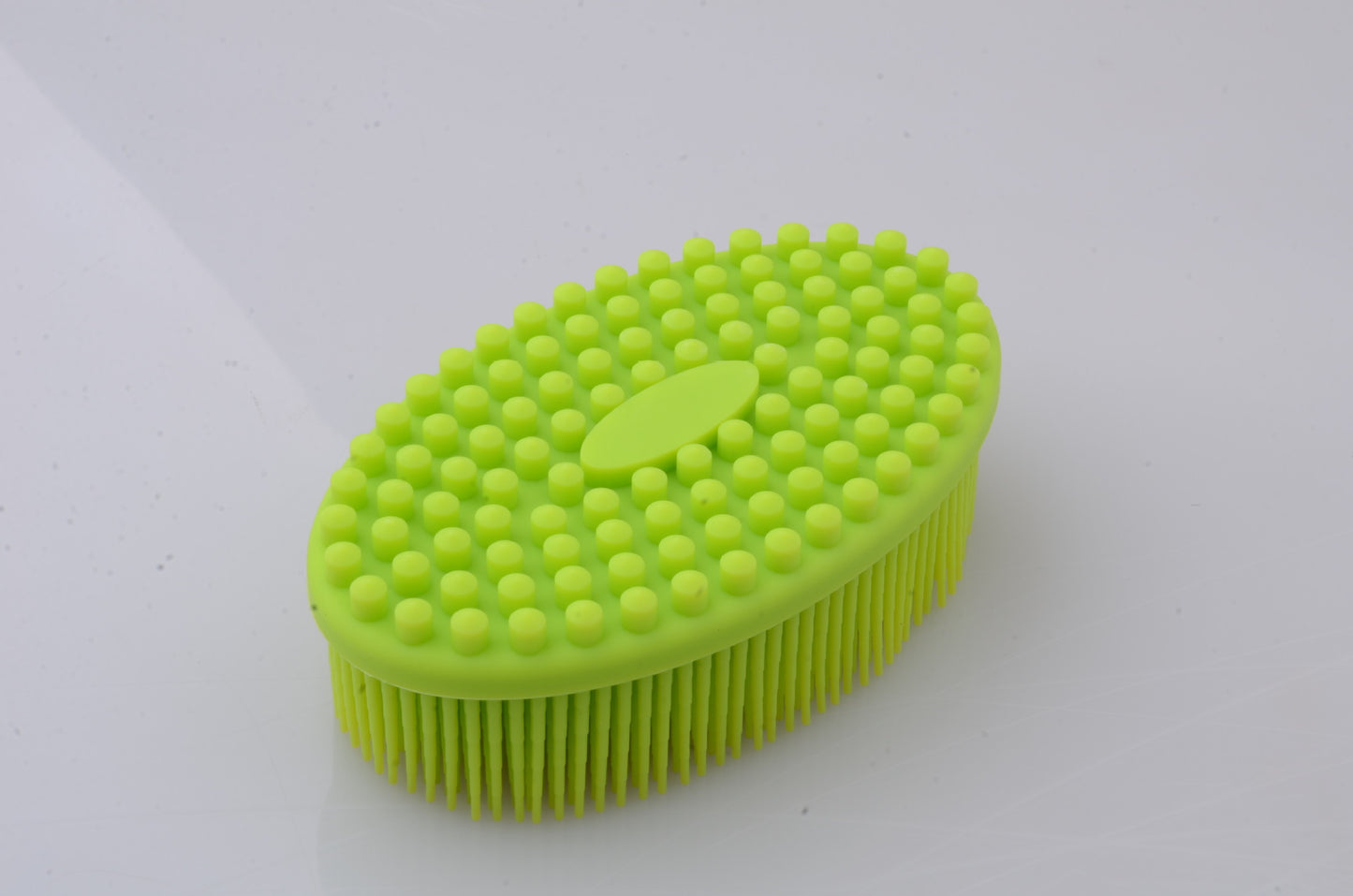 Bright green silicone scrub brush with a textured surface featuring evenly spaced round nubs on top and long bristles on the bottom, placed against a smooth white background.