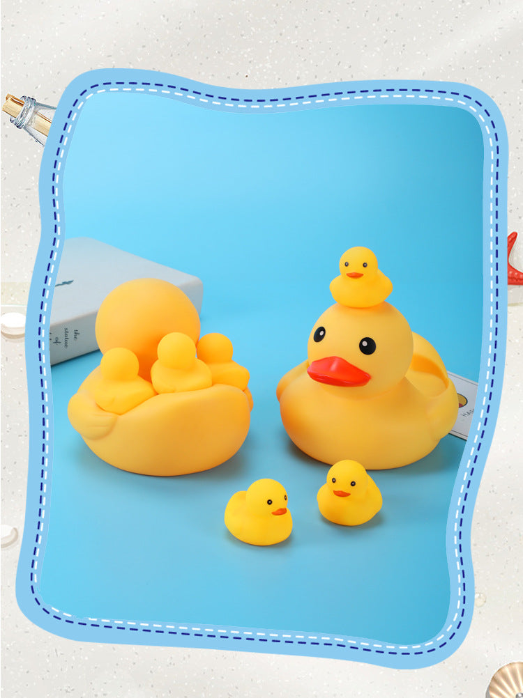 Yellow rubber duck family on a blue background. One large duck with a baby duck on its head and four small ducks around. A book is partially visible on the left.