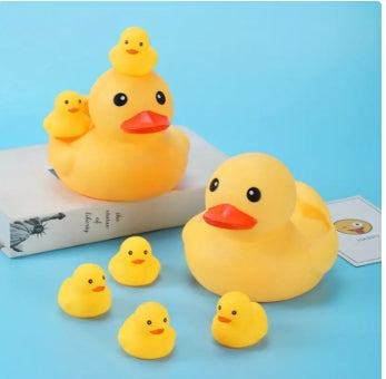 Yellow rubber ducks of various sizes on a blue surface. Two large ducks are each topped with a smaller duck, while four smaller ducks are scattered around. A book is partially visible.