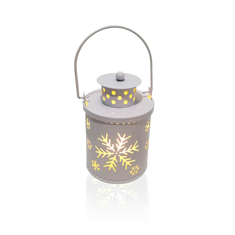 White metal lantern with a handle, featuring illuminated snowflake and dot cutouts, casting a warm glow. The cylindrical design reflects a festive, cozy ambiance.