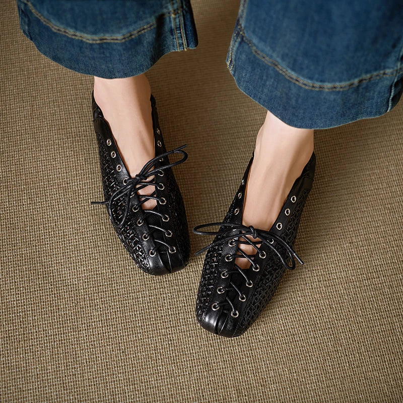 Person wearing black, woven lace-up shoes with silver eyelets, paired with cropped denim jeans. The background is a beige textured surface.
