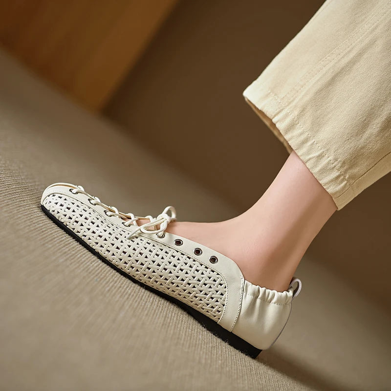 Beige woven slip-on shoe with lace details and elastic back, worn by a person in matching beige pants on a carpeted floor.