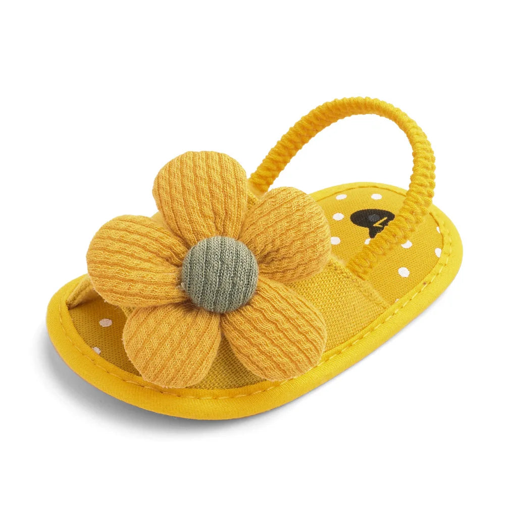 Yellow baby sandal with a knitted flower on top, polka dot inner sole, and an elastic back strap.