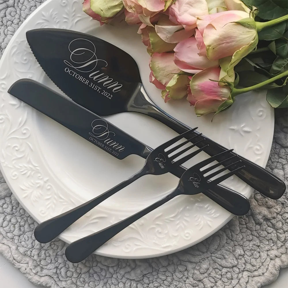 Elegant black cutlery set engraved with "Dunn" and date, displayed on a decorative white plate with pink roses, resting on a textured gray surface.