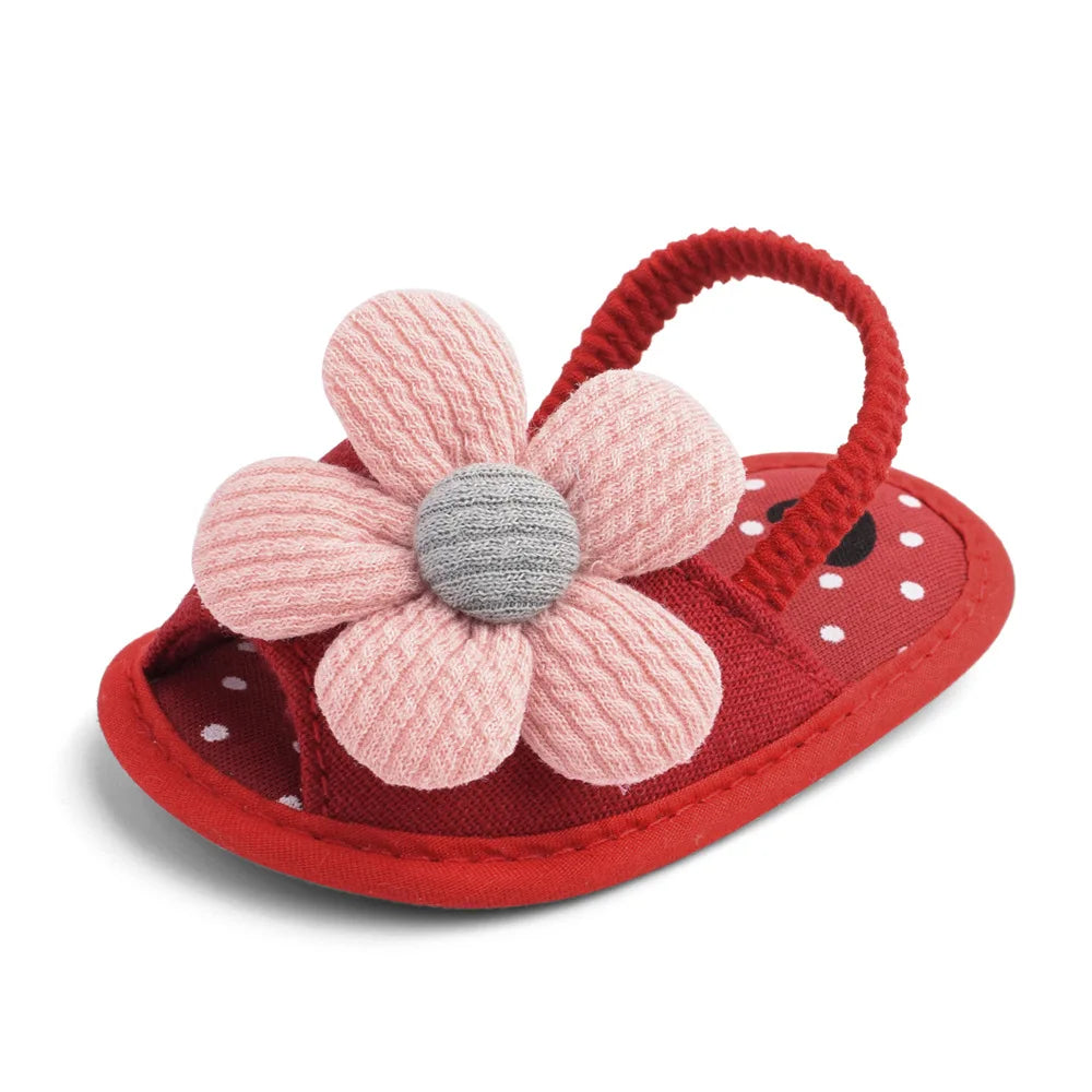 Red baby sandal with a pink knitted flower on top, featuring a red strap and white polka dots on the sole.