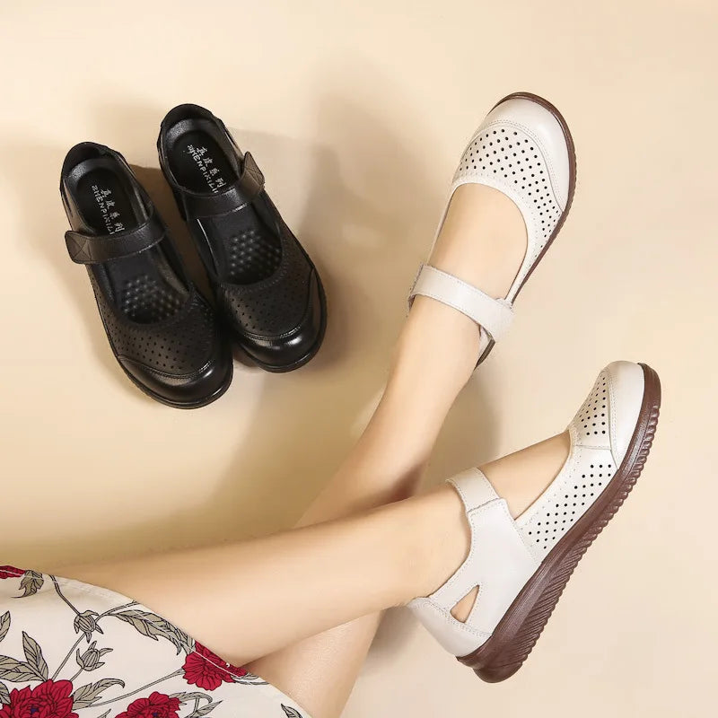 A pair of legs wearing white perforated Mary Jane shoes with brown soles rests on a beige background. Nearby, a pair of black perforated Mary Jane shoes sits side by side.