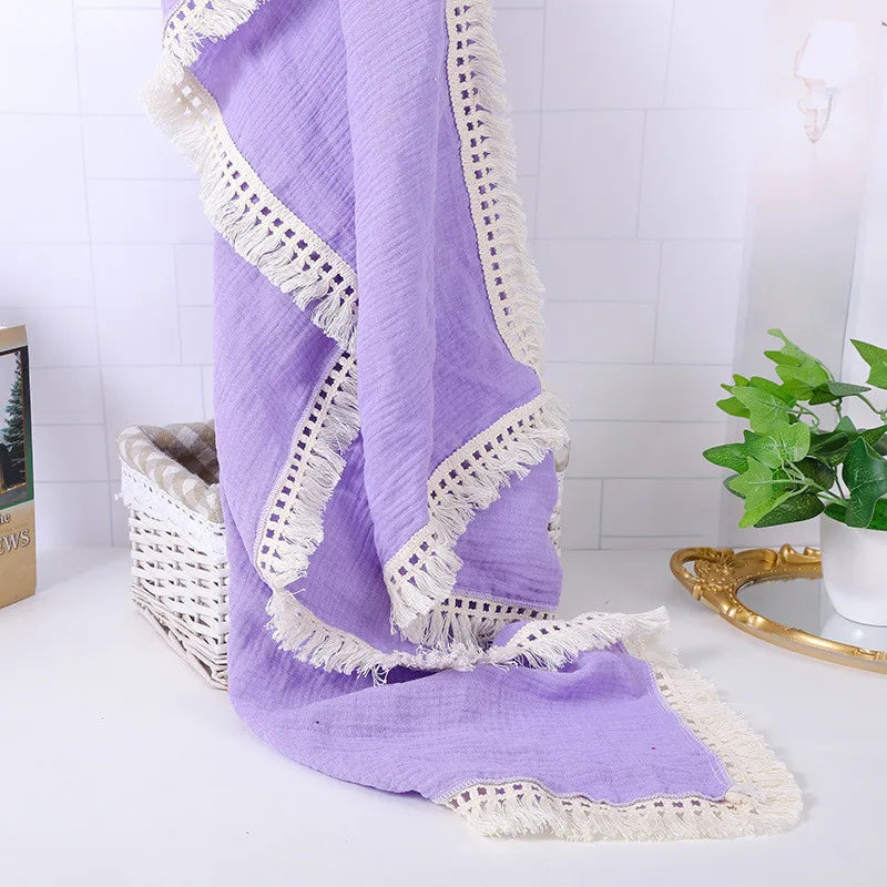Purple fabric with white lace borders drapes over a wicker basket. A green plant and a gold mirror accent the white tiled background, creating a cozy, elegant setting.