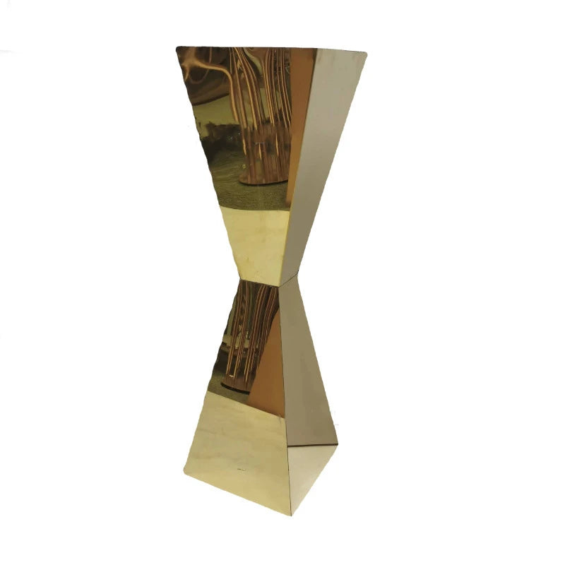 A golden, twisted, mirror-finished sculpture with a narrow midsection and wider top and bottom, reflecting parts of its surroundings, including abstract patterns.