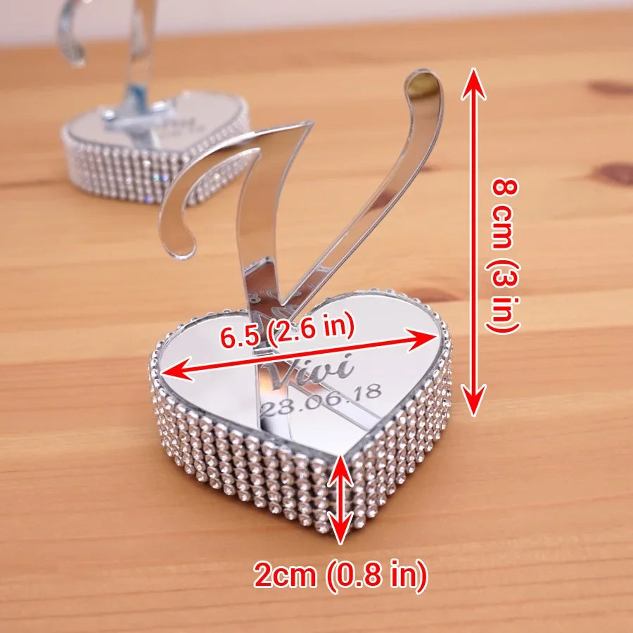 Heart-shaped silver holder with rhinestone border, personalized with "Vivi 28.06.18." Measures 8 cm high, 6.5 cm wide, and 2 cm deep. Placed on a wooden surface.