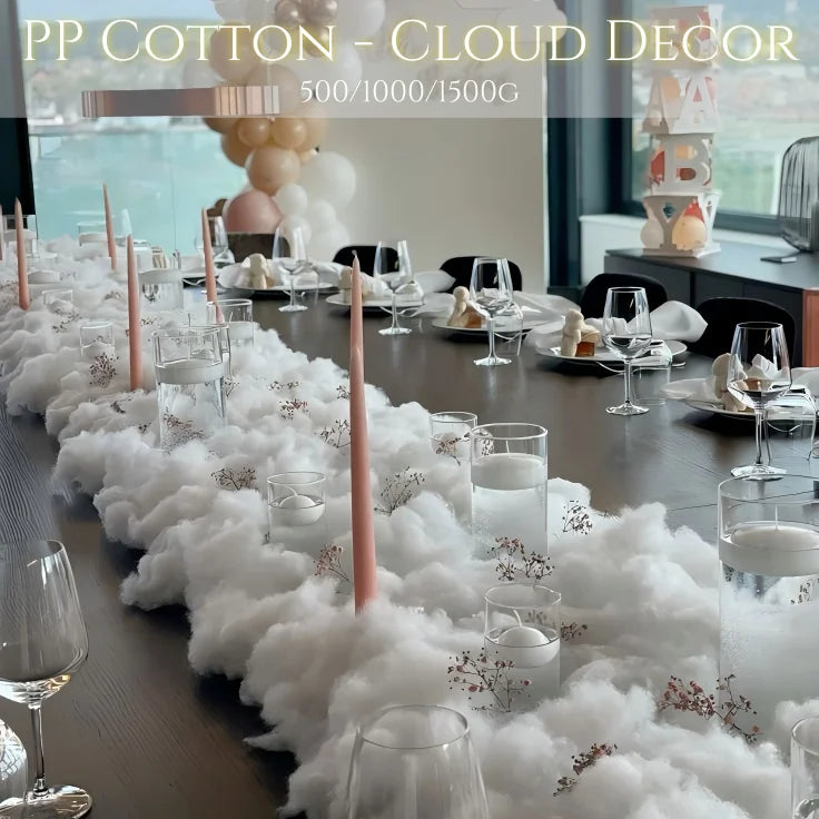 Elegant dining setup with a long table featuring cloud-like cotton decor, pink candles, and glassware. Background includes stacked decor and balloons. Text reads "PP Cotton - Cloud Decor."