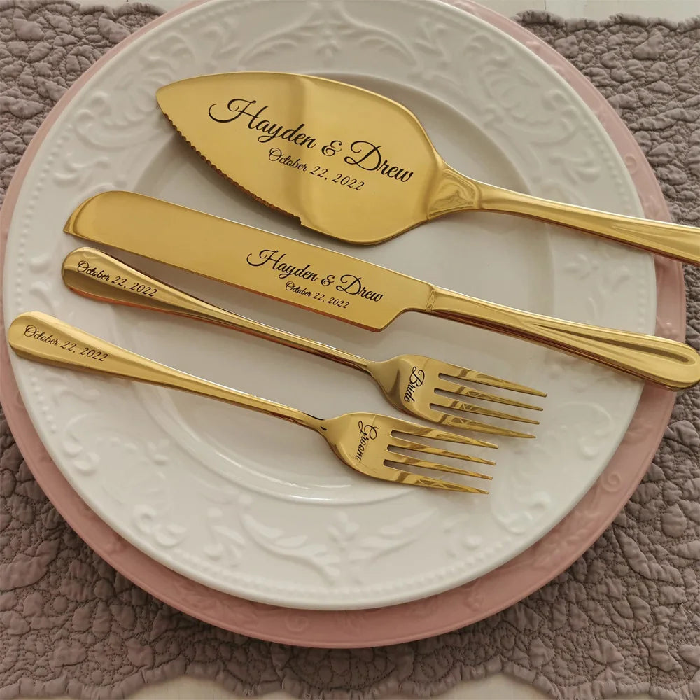 Gold cake server set with "Hayden & Drew, October 22, 2022" engraved, resting on stacked pink and white plates with a textured placemat underneath.