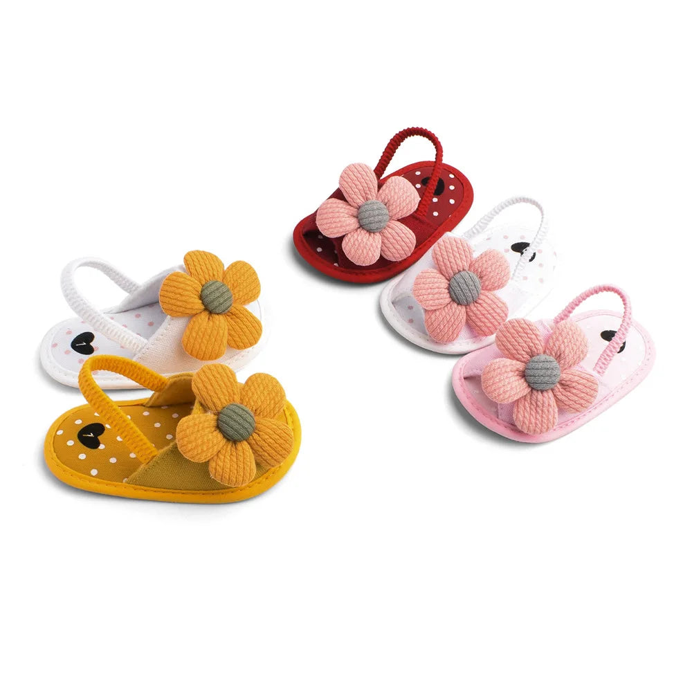 Colorful baby sandals with large textured flower designs in yellow, red, and pink against a white background. Each sandal features polka dots and heart accents.