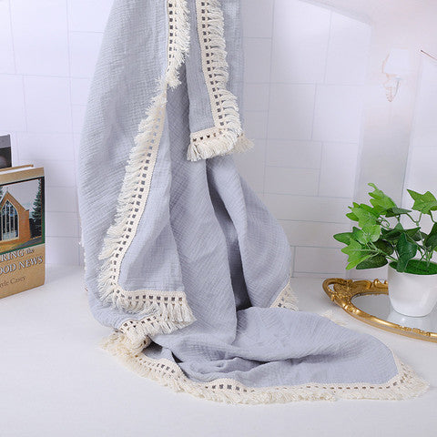 A soft gray fabric with cream lace edges drapes elegantly over a white tiled background. Nearby are a gold mirror, green potted plant, and a book titled "Good News."
