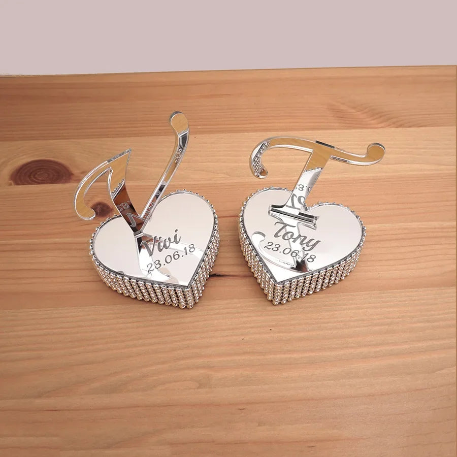 Two silver heart-shaped table ornaments with rhinestone edges, engraved with "Vivi" and "Tony" above the date 23.06.18. Initials "V" and "T" stand upright on each heart.