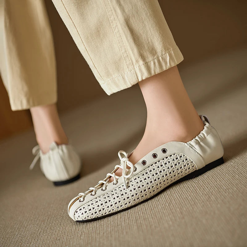 Person wearing beige pants and stylish white leather loafers with a woven design and black soles, walking on a textured carpet.