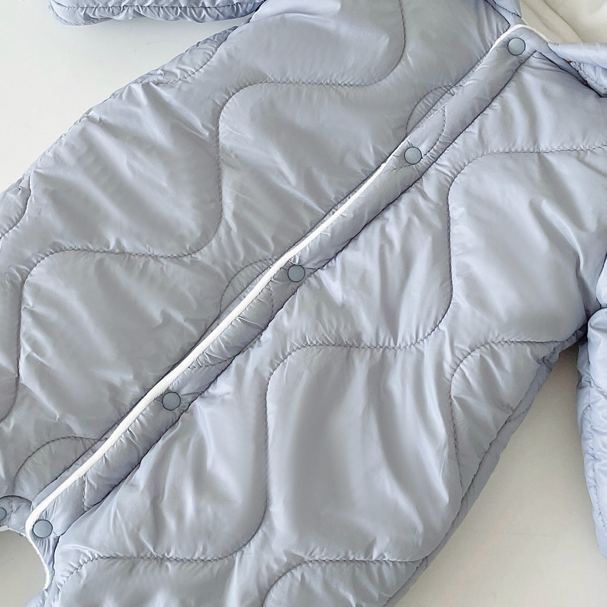 Light blue quilted jacket with a wavy stitched pattern and snap button closure, displayed on a white surface. Warm, padded design suitable for cold weather.