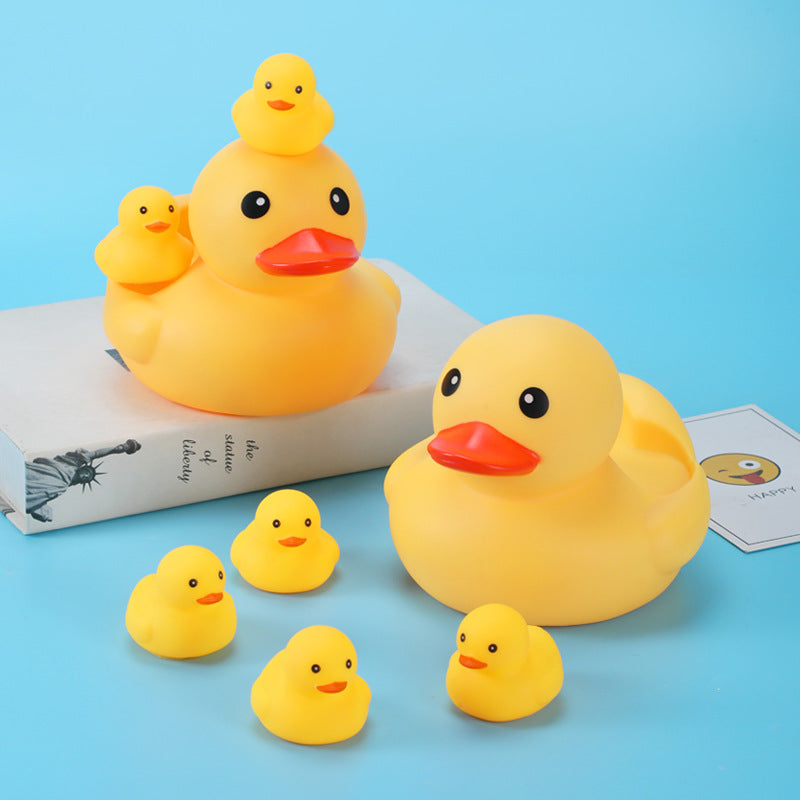 Yellow rubber ducks, including two large ones with smaller ducklings on their backs, are displayed on a book and a blue surface, creating a playful arrangement.