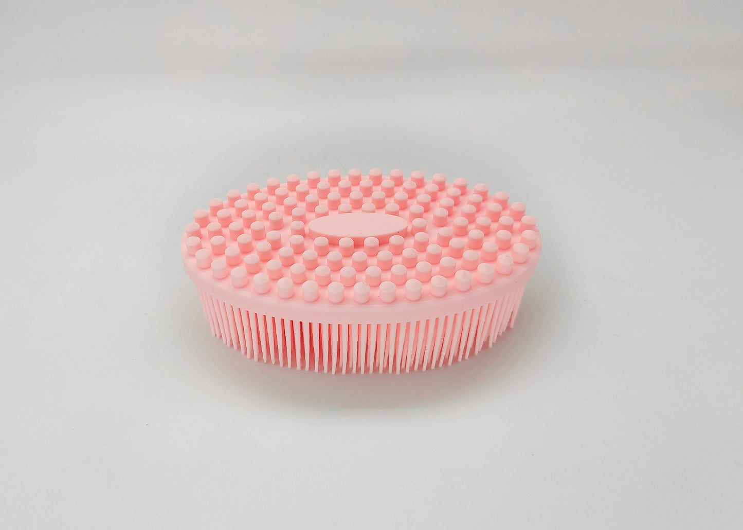 Pink silicone bath brush with a round shape, featuring soft, short bristles on top and longer bristles on the sides. Designed for gentle exfoliation and cleansing.