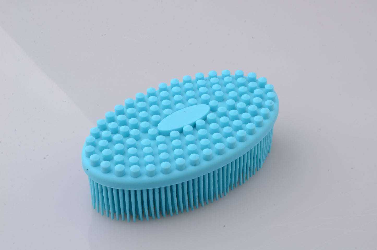 Blue oval silicone brush with bristles on one side and textured bumps on the other, designed for cleaning or massage, placed on a plain white surface.