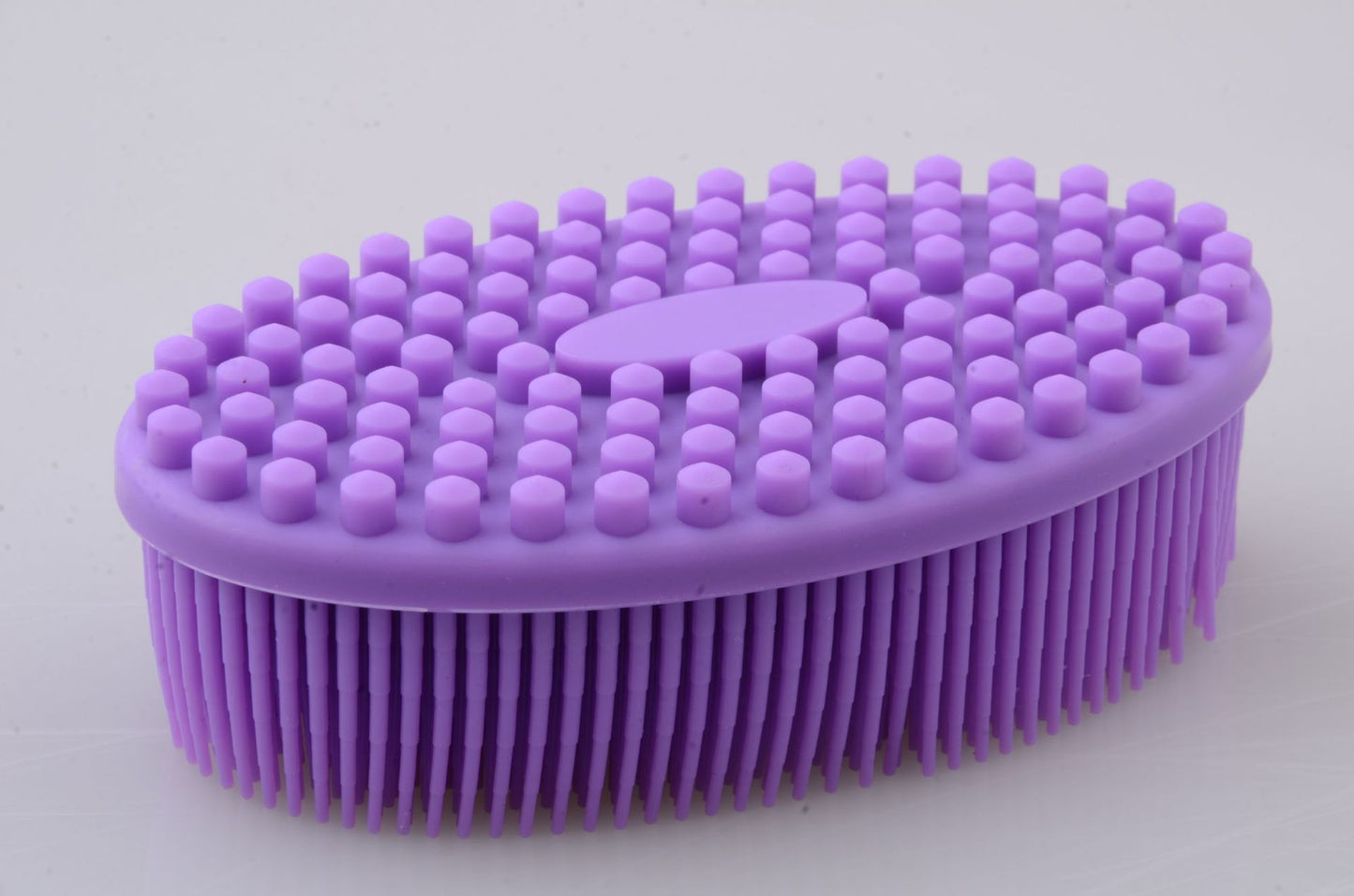 Purple silicone oval brush with a textured top of hexagonal bumps and a base of flexible bristles, designed for use on hair or skin, on a plain background.