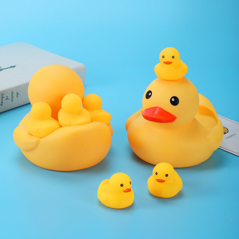 A collection of yellow rubber duck toys with one larger duck holding three smaller ducks, and another large duck with one duckling on top. Two ducklings are in the foreground.